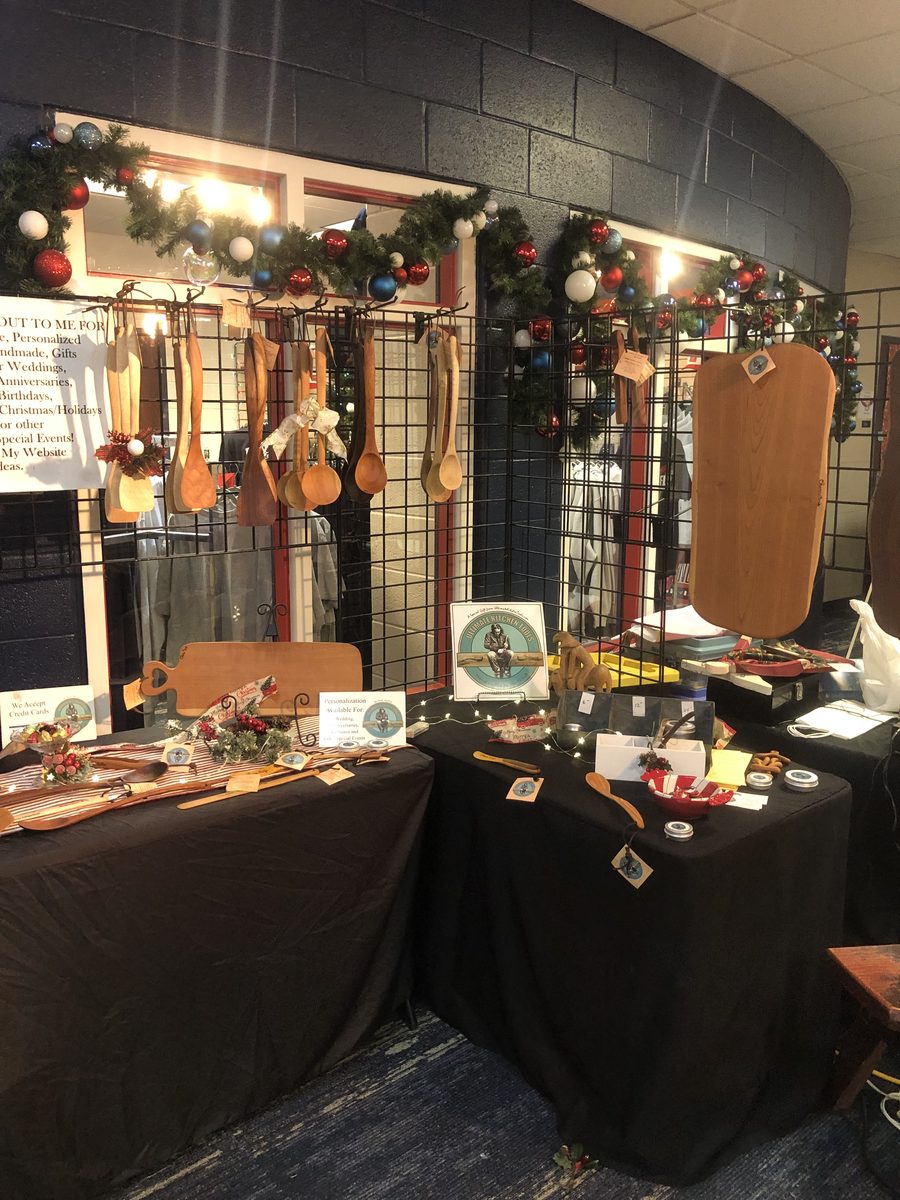 The Ultimate Kitchen Tools booth at a holiday show, with garland and ornaments above the hanging spoons and boards