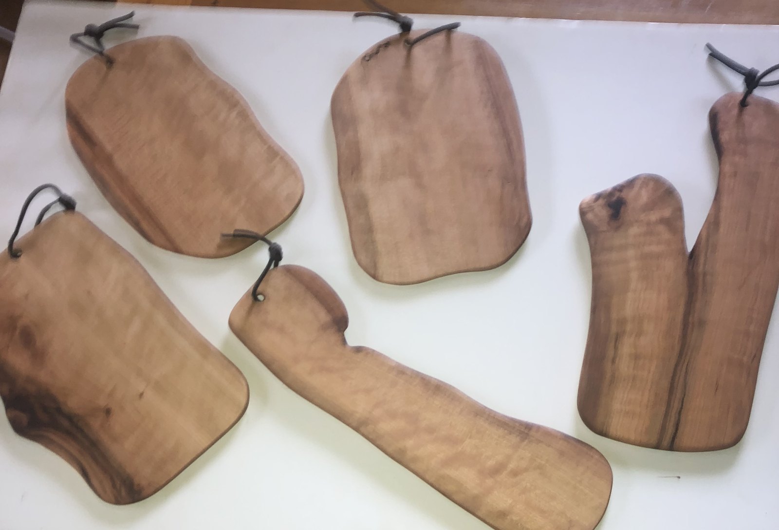 Five small hand-carved cheese boards with leather hanging loops, laid out together, each a different shape
